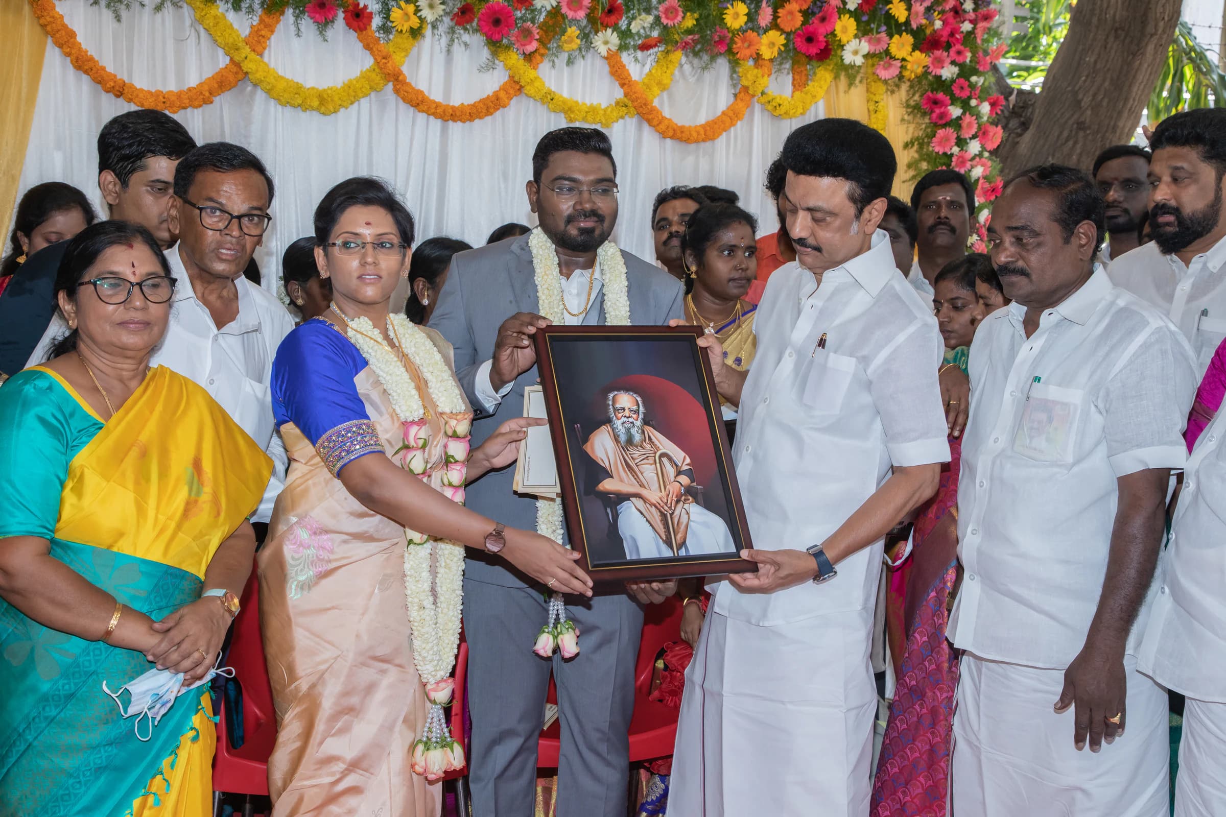 Priya and others presenting a framed portrait at a wedding gathering